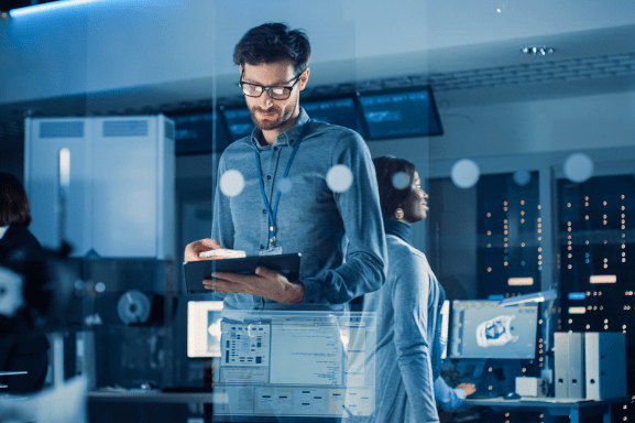 A Managed IT Services professional reviews notes in a server room with other IT professionals in the background.