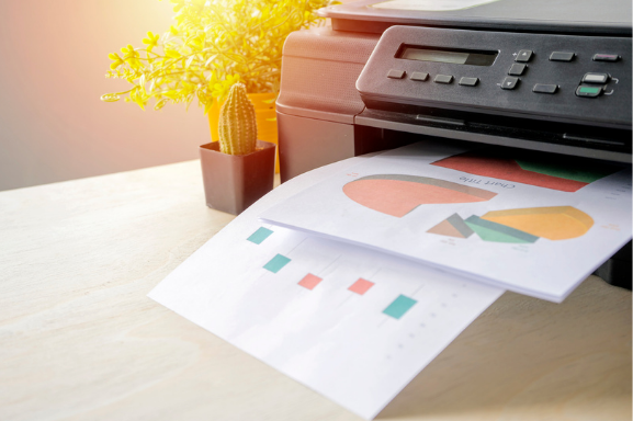 Close up of an office printer with colorful charts in the output tray to signify Managed Print Services.