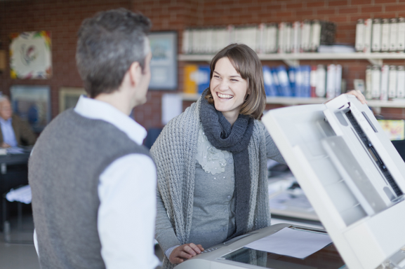 Two business professionals stand next to a copier smiling, signifying office copiers
