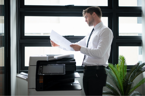 A professional stands in front of a copier examining the output with a questioning expression, signifying the importance of office copiers.