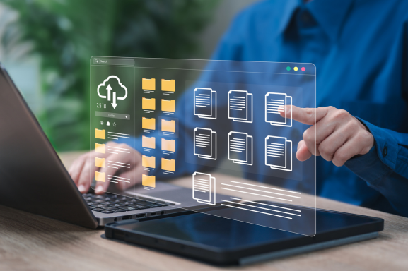 Close up of an office worker typing on a laptop with an overlay of a file manager with icons of documents, file folders, and a cloud download signifying enterprise document workflow solutions.