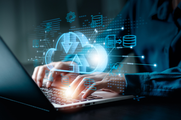 Close up of a professional at a laptop in a dark setting with icons of a cloud backup with file and server and gear icons around it signifying backup and data protection.