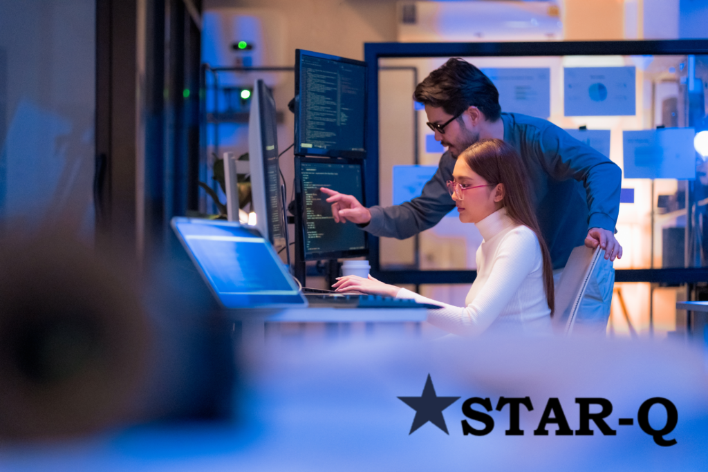 Two IT employees in an office discussing code on a screen with the Star-Q icon in the bottom right