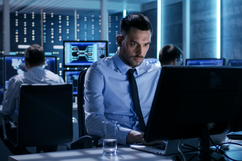 IT office workers in a dark, bluish company business setting in front of laptops and computers with servers in the background
